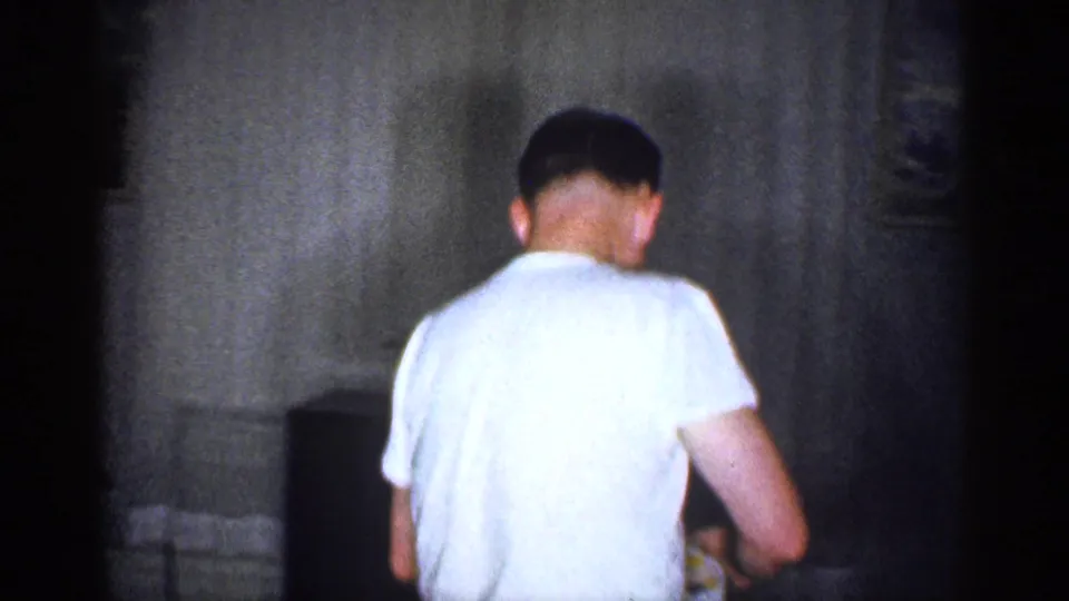 1959 Michigan home-movie frame showing an adult man from behind near a cabinet-style television in a private living room.