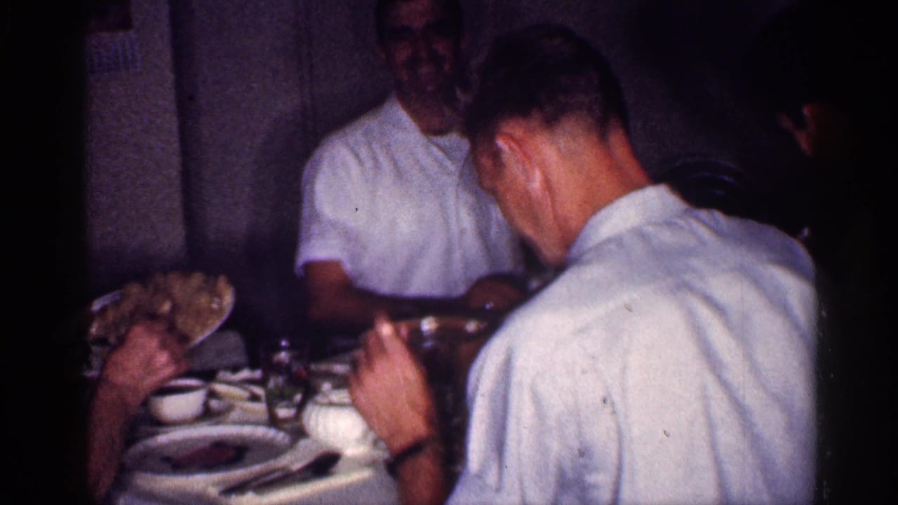Adults seated around a dining table with plates and cups in a dim room.