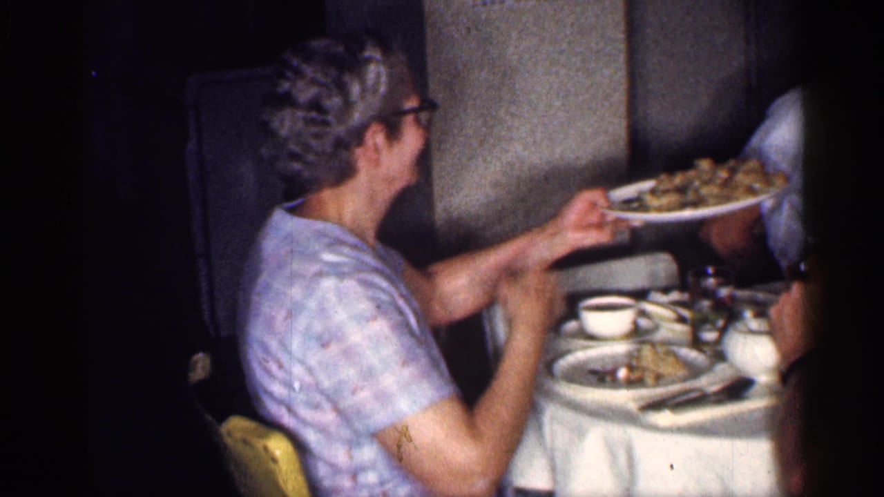 Woman in a patterned blouse passes a plate across a dining table.