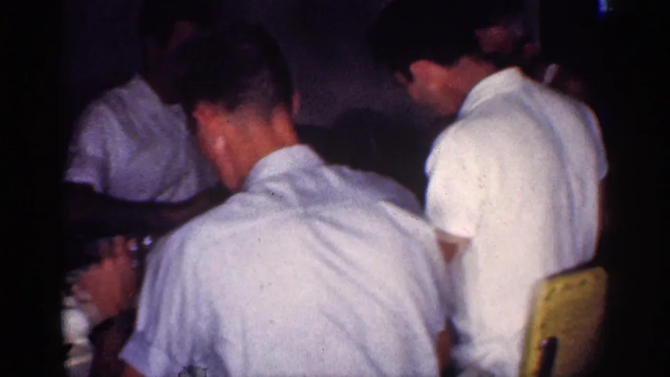 Men in short-sleeved white shirts sit around a Michigan dining table in this 1959 home-movie frame.