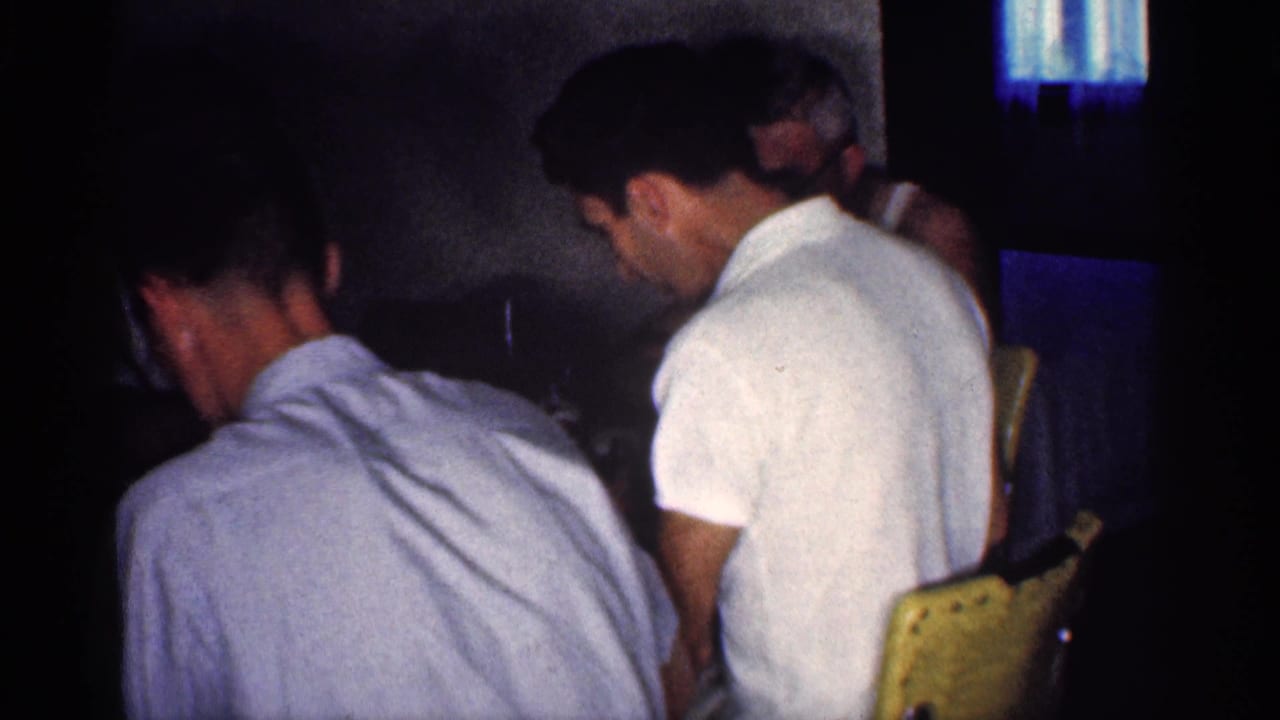 Men in short-sleeve shirts sit at a dining table in low light.