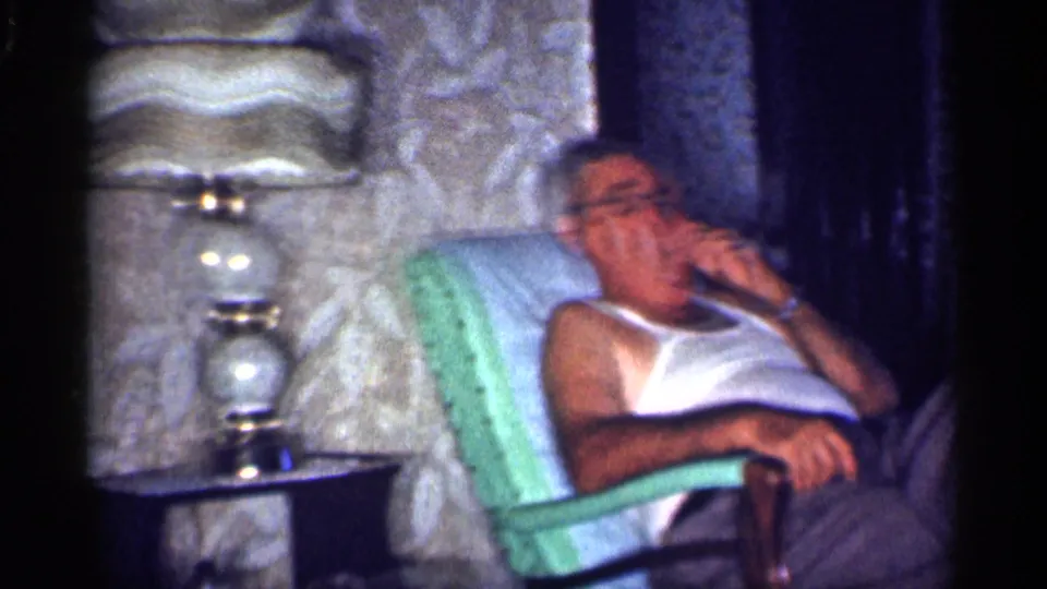 Soft 8mm frame of a man resting in a green armchair in a 1959 Michigan private interior.