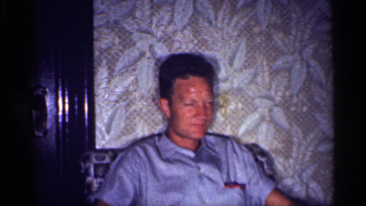 1959 Michigan interior frame showing an adult man in a light blue short-sleeve shirt seated in a vintage living room.