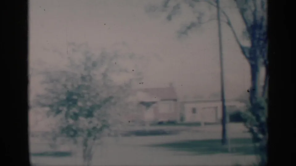 Faded 1959 Michigan 8mm frame with a distant house, lawn, shrubbery, and a tall tree near the right edge.