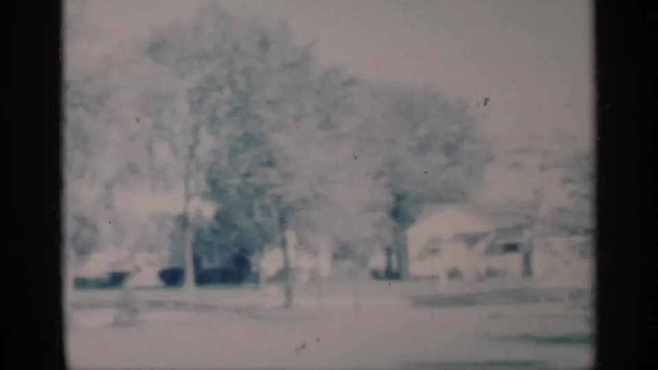 1959 Michigan suburban exterior with leafless trees, snow on the ground, modest homes, and a partly visible parked car.