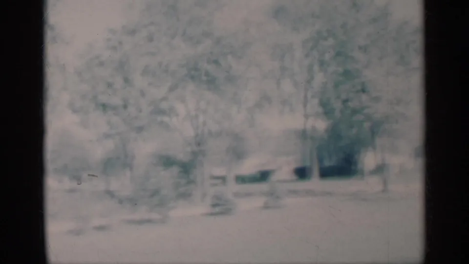 Soft 1959 Michigan home-movie frame with snow, trees, and houses seen from a fixed residential vantage point.