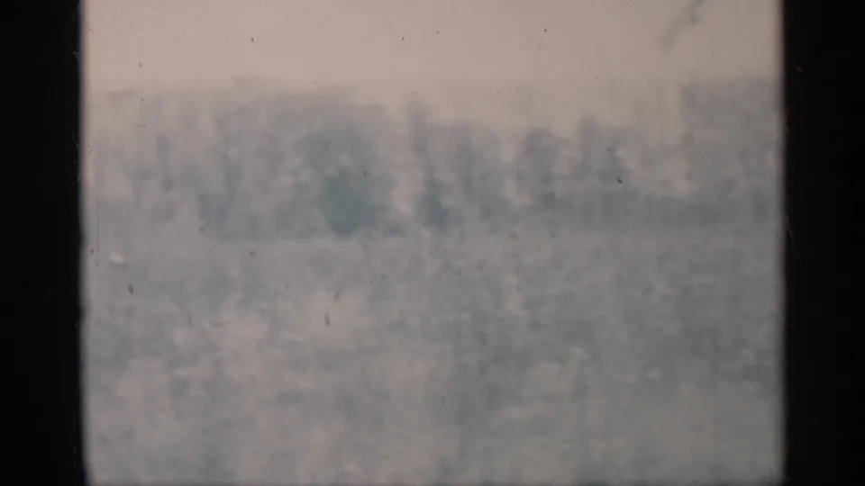 Faded 8mm frame of a soft, overexposed outdoor landscape, with only faint tree or brush shapes visible.