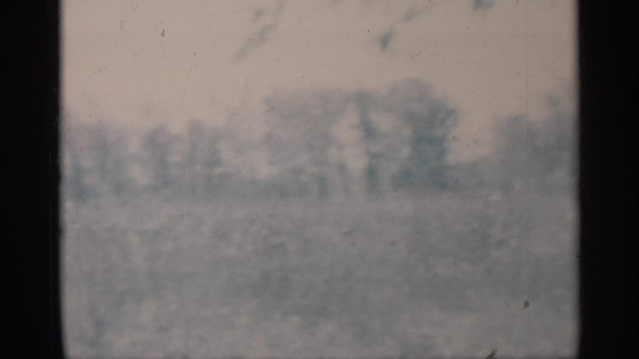 Hazy 1959 Michigan 8mm frame with distant trees and open grass seen through dark vertical film borders.