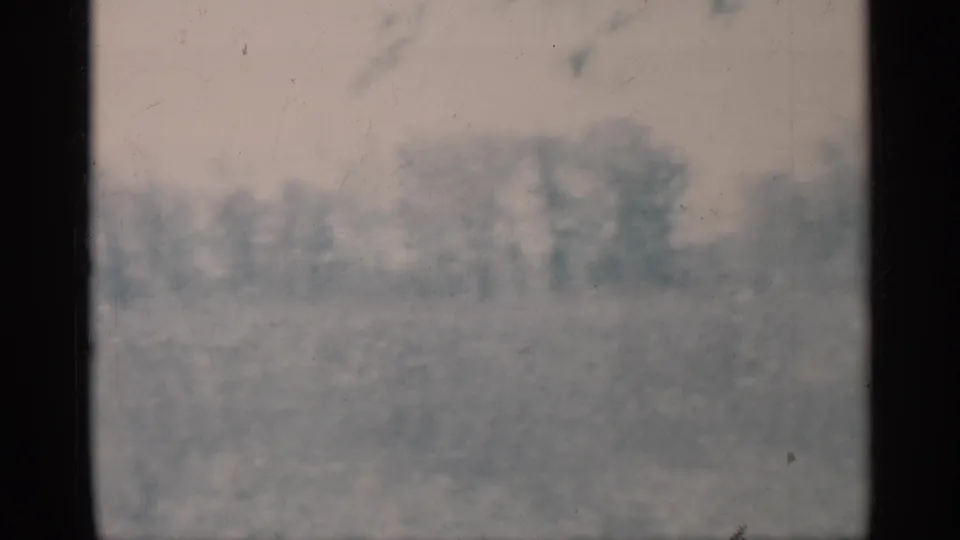 Hazy 1959 Michigan 8mm frame with distant trees and open grass seen through dark vertical film borders.