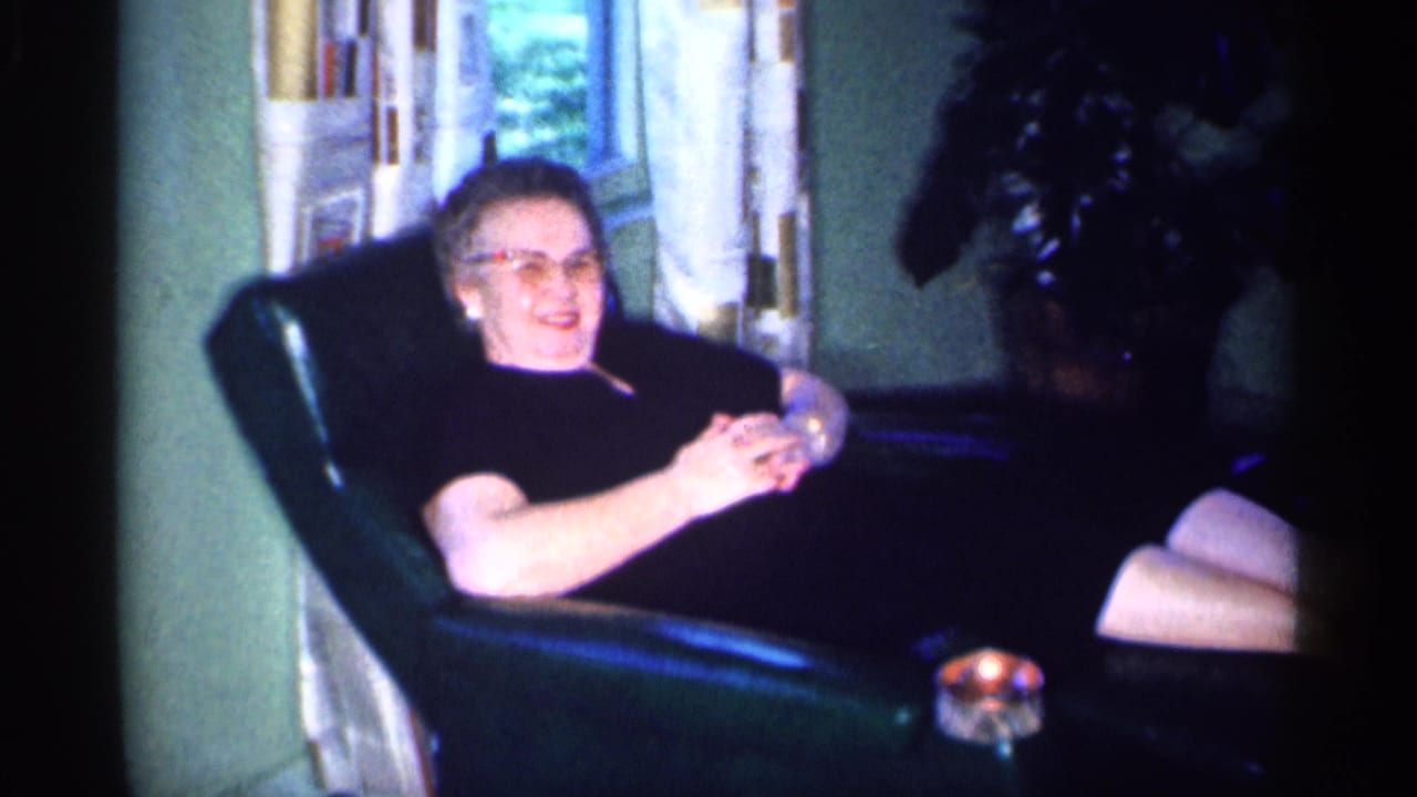 Woman in glasses reclines in a green armchair beside a small glowing object.