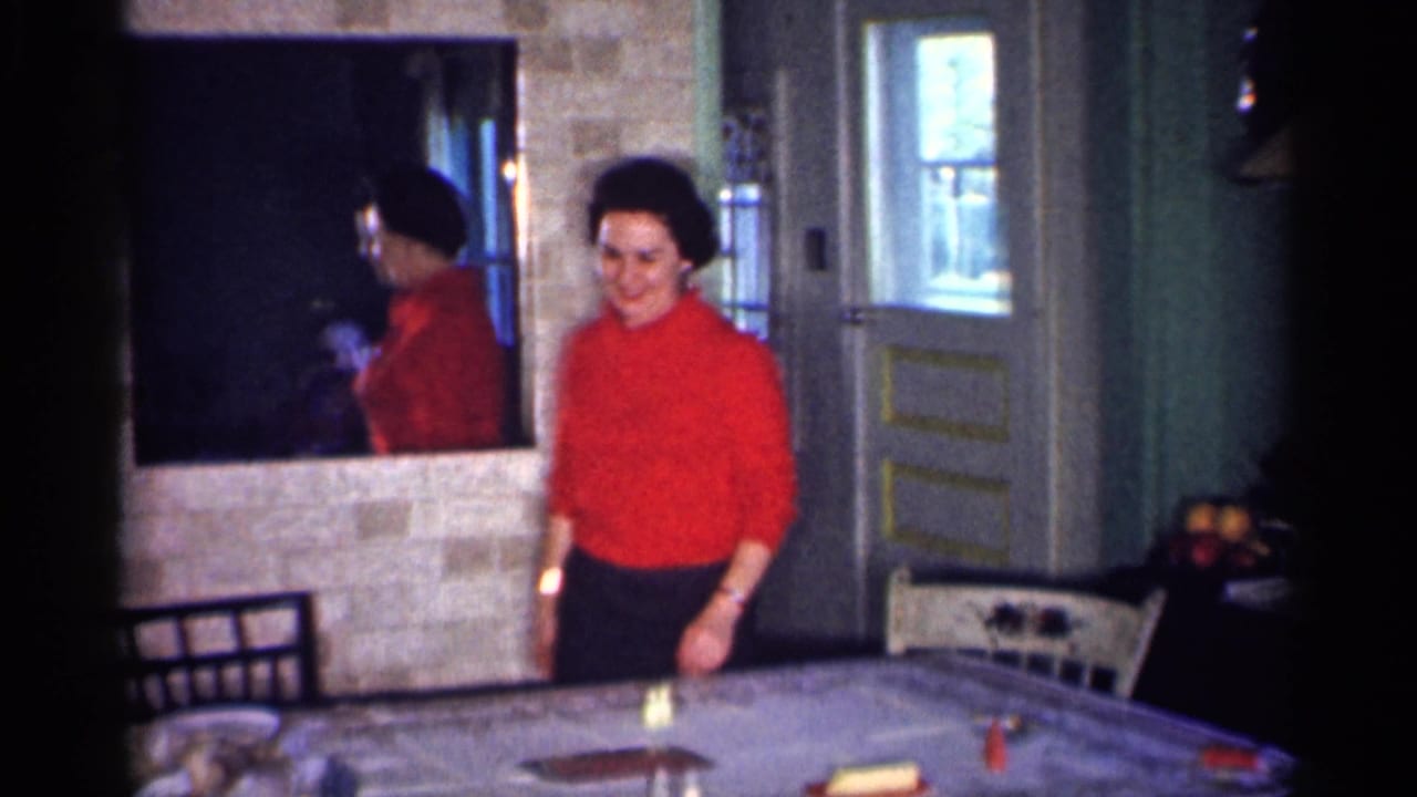 Woman in a red top stands beside a dinner table in a home interior.