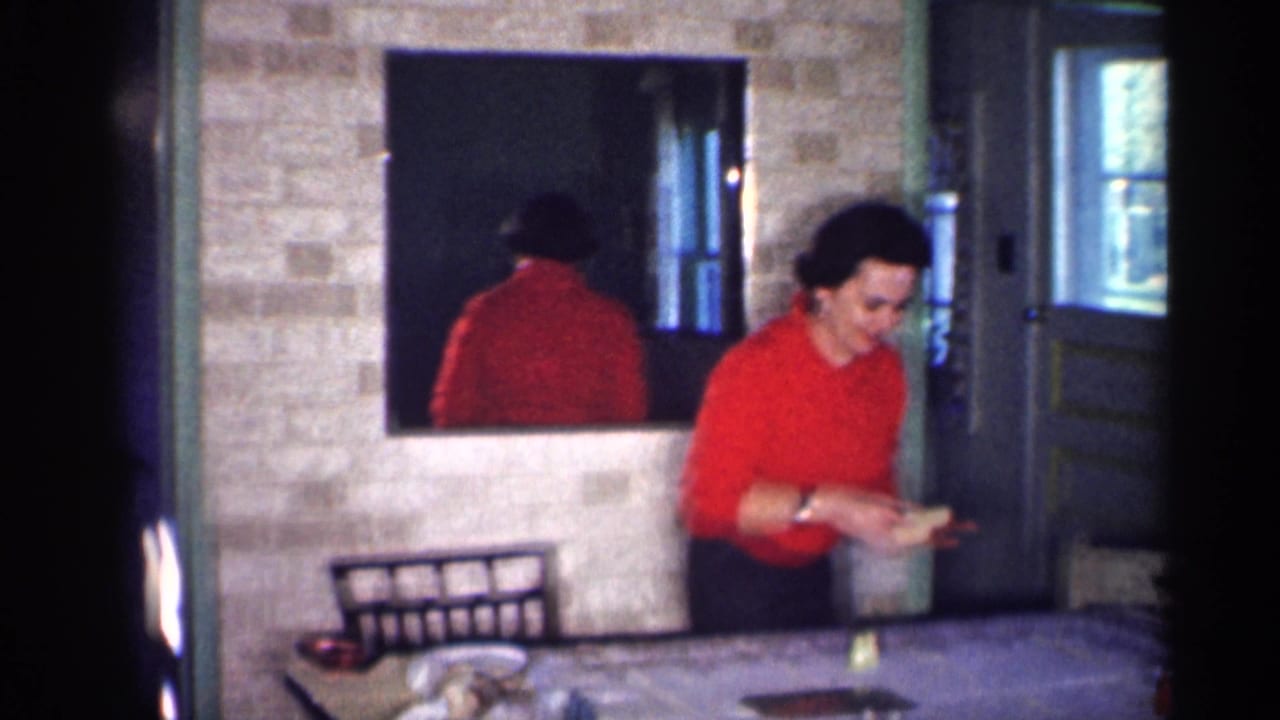 A woman in a red top clears items from a dinner table in a 1959 Michigan private home interior, with her reflection visible in the mirror.