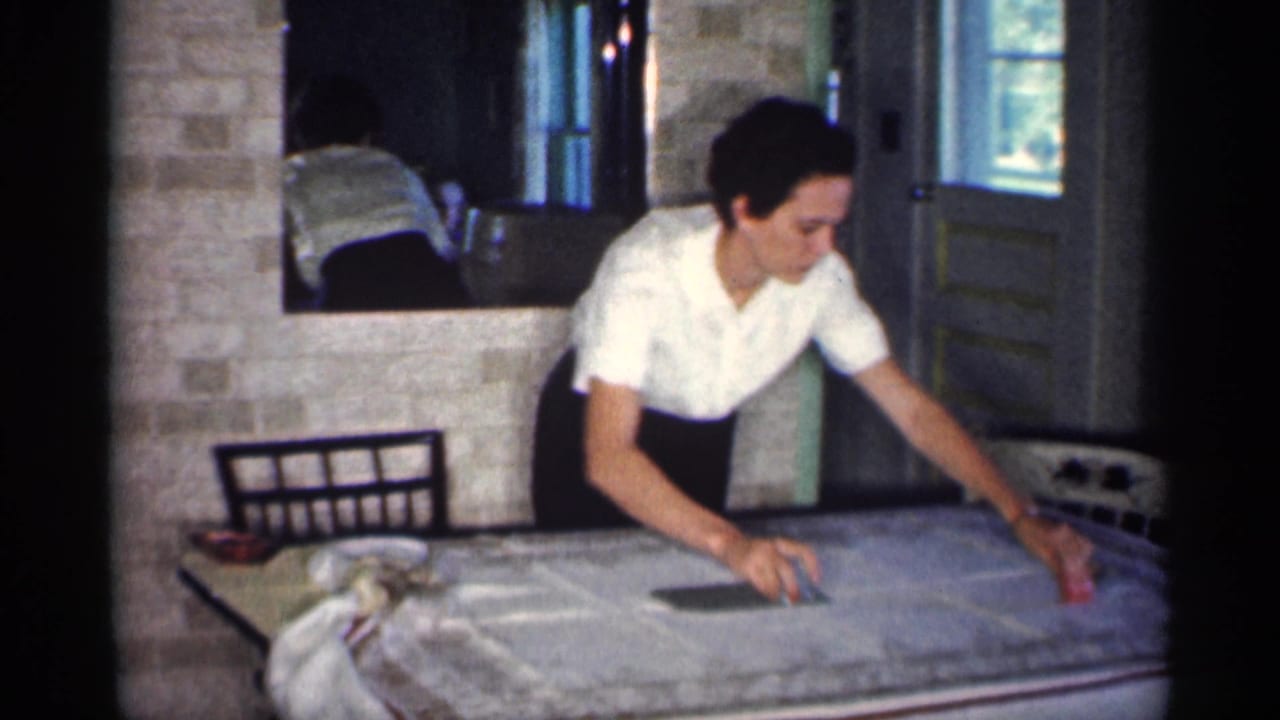 Woman in a white blouse irons a cloth on a table in a brick-walled home interior.