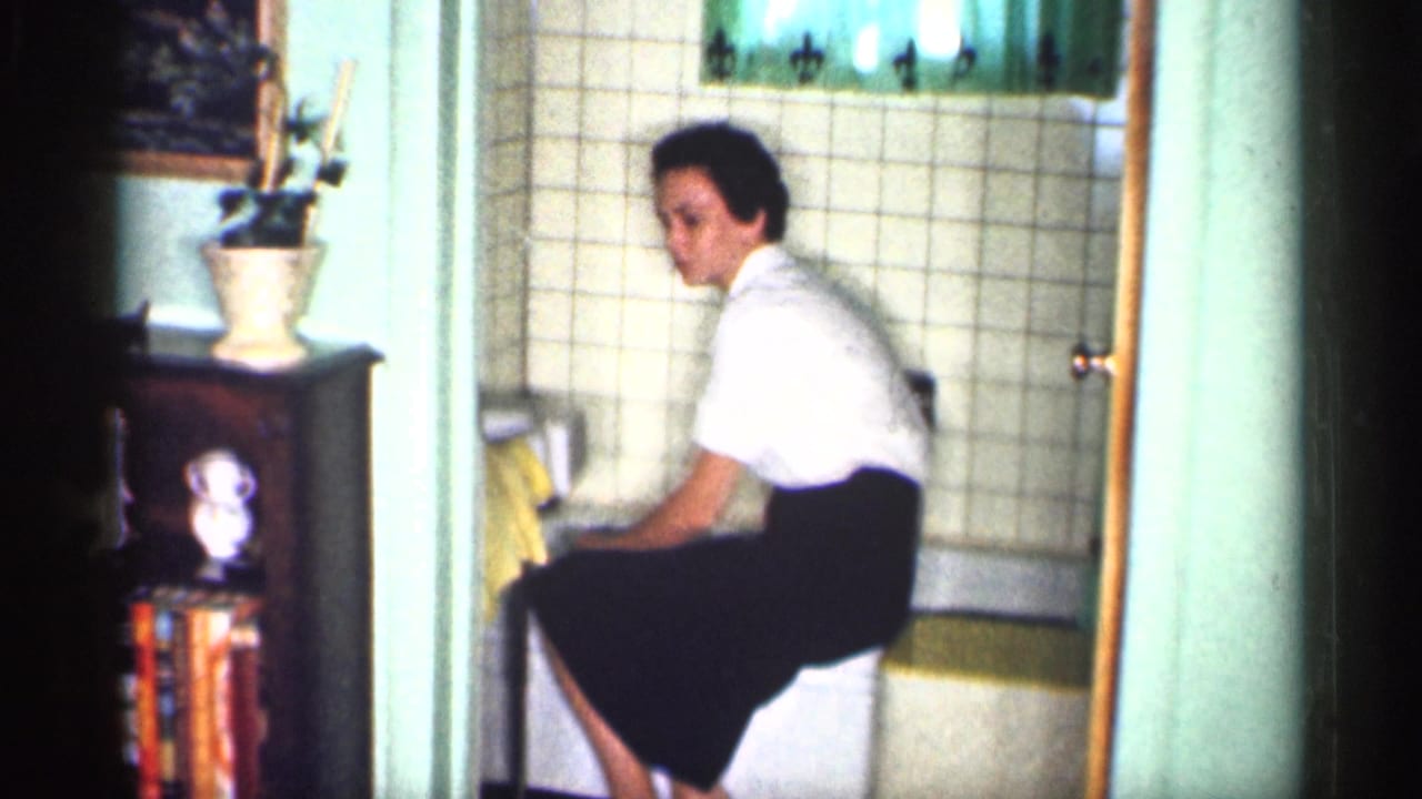 Woman seated beside a bathtub holding a yellow cloth in a tiled bathroom.