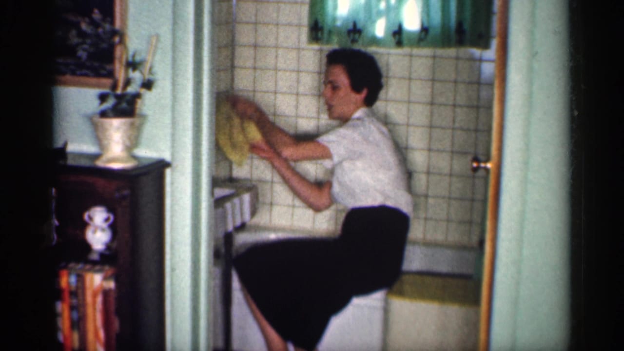 Woman wipes the tiled bathtub wall with a yellow cloth.