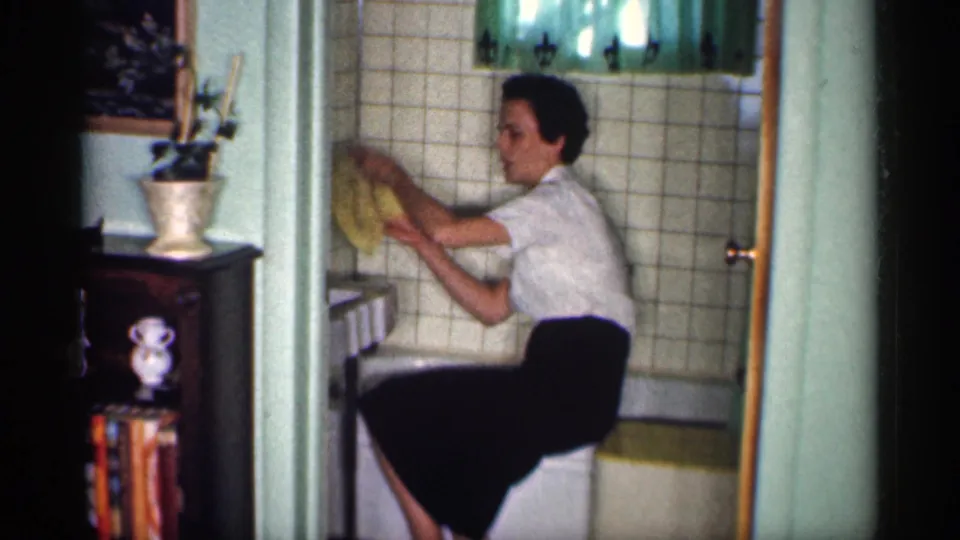 The woman raises a yellow cloth to scrub the tiled wall above the bathtub in the Michigan bathroom scene.