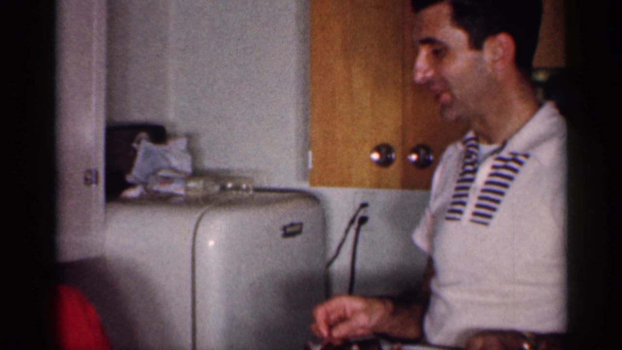 Man in a white striped polo stands near a rounded refrigerator and kitchen cabinets.