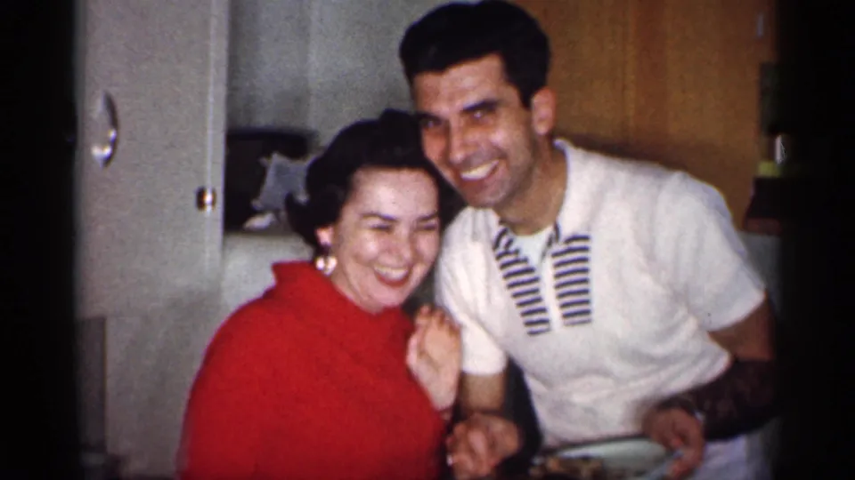 In a 1959 Michigan kitchen, a woman in a red sweater and a man in a white striped polo smile close together.