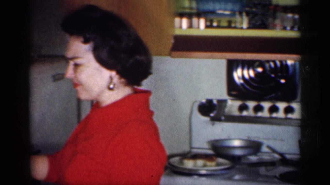 Woman in a red dress standing at a kitchen stove with cookware nearby.