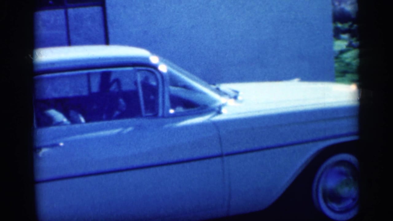 White vintage sedan seen from the side with a person visible through the window.