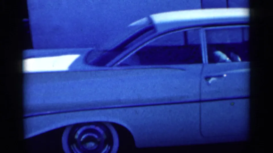 Close 8mm view of the white sedan's side, showing chrome trim, front door, whitewall tire and soft blue film color.