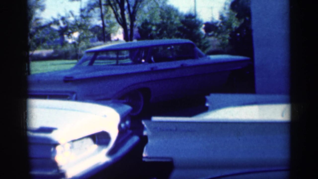 White sedan front end overlaps a light station wagon by a grassy yard.