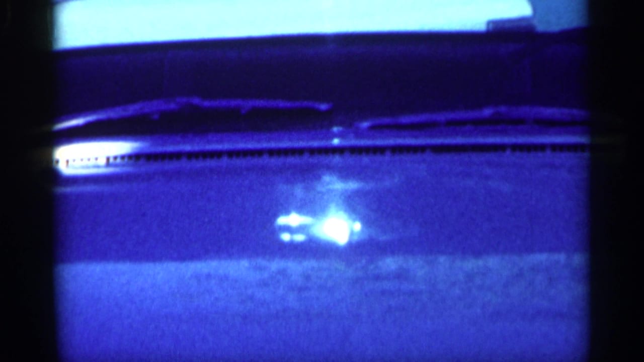 Close view of a car windshield and hood with wipers visible in strong blue-tinted light.