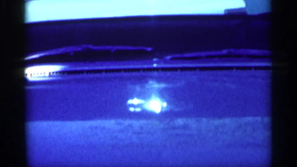 1959 Michigan 8mm frame showing a close view of a parked car windshield, hood, wipers, and reflected light.