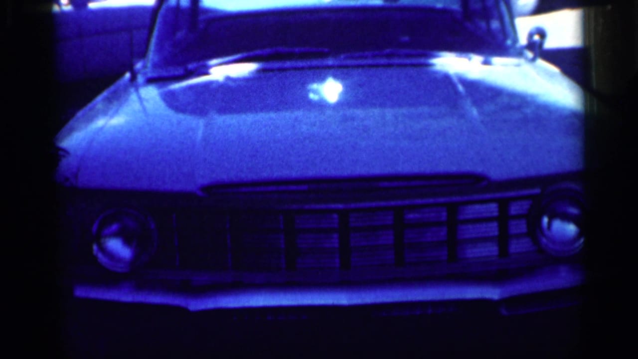 1959 Michigan home-movie frame showing the front end of a parked car with chrome grille, hood, and round headlights.