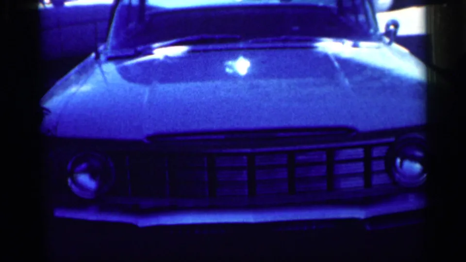 1959 Michigan home-movie frame showing the front end of a parked car with chrome grille, hood, and round headlights.
