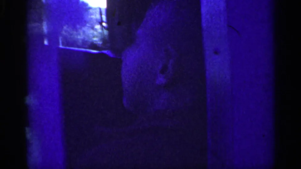 Shadowed close-up of a person's face in the 1959 8mm Michigan footage, with features partly obscured by blue cast and darkness.