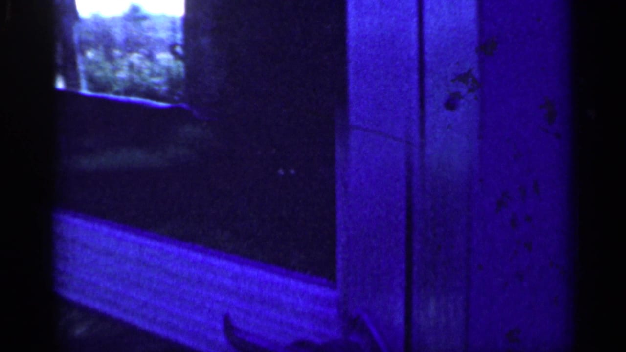 Dim blue-toned interior with a bed or couch at left and dark vertical doorway area.