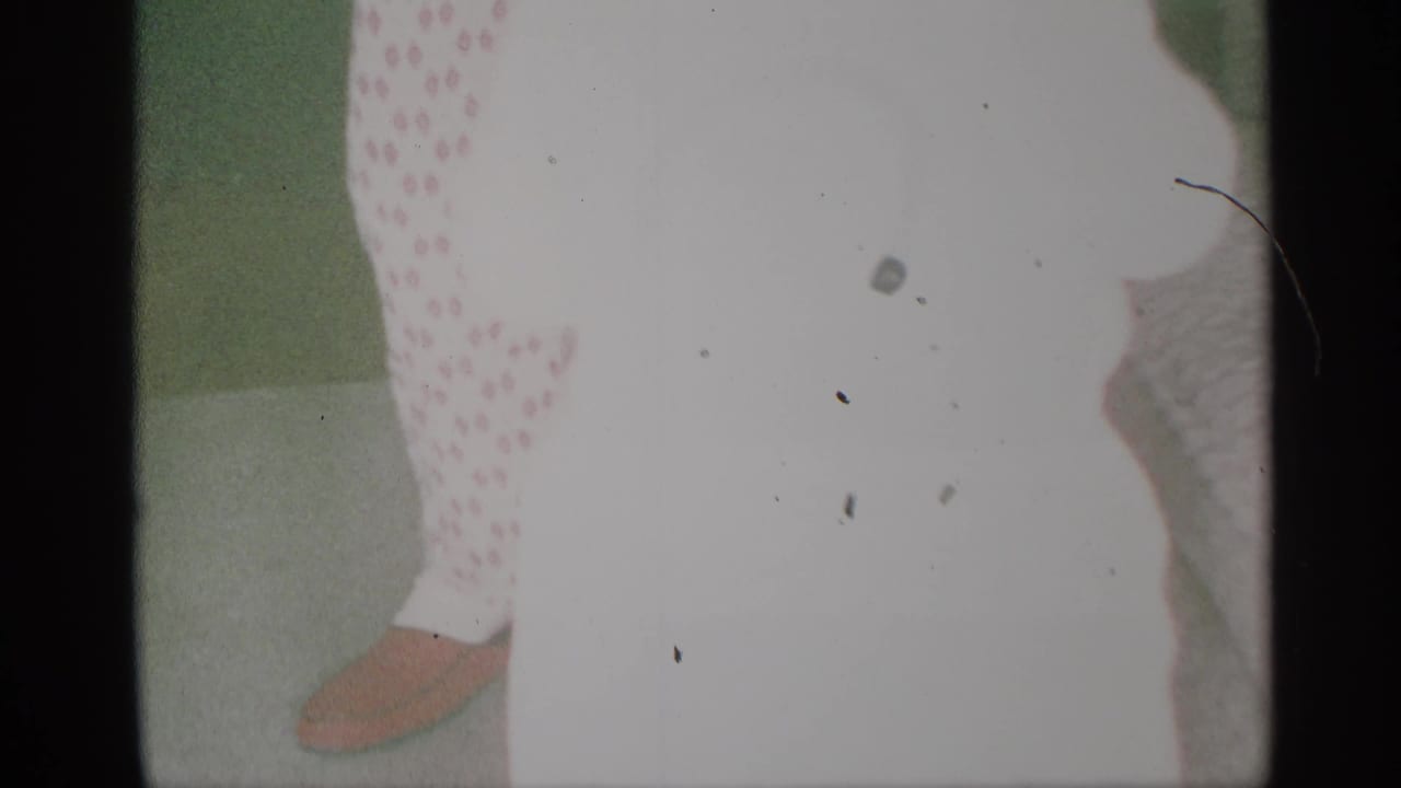 Small child in polka-dot clothing near a green wall, with brown shoes visible.