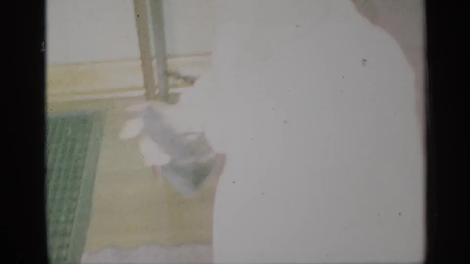 Overexposed 1959 New York home-movie frame with a cropped person near a pale interior doorway or wall edge.