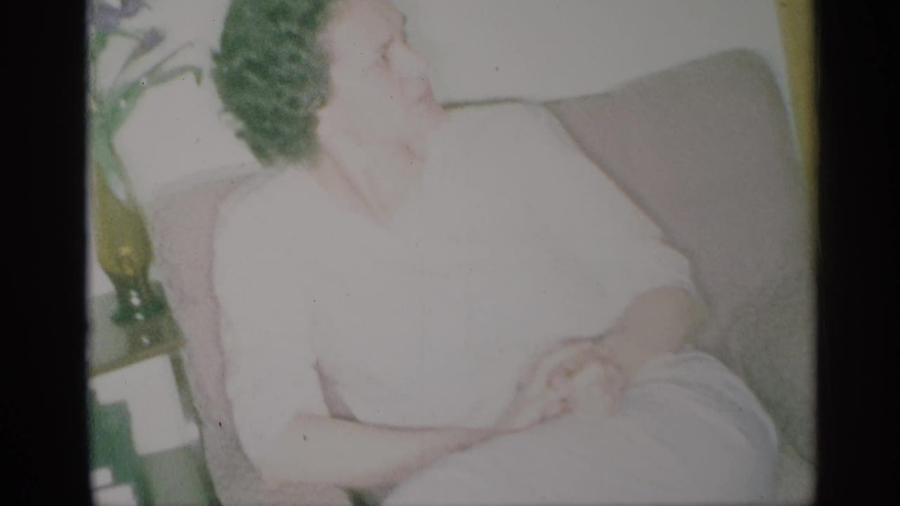 Woman in a white dress sits in a tan armchair with her hands clasped.