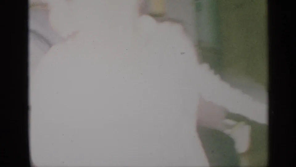 Faded 1959 New York home-movie frame with the child close to the camera in a bright, overexposed room.