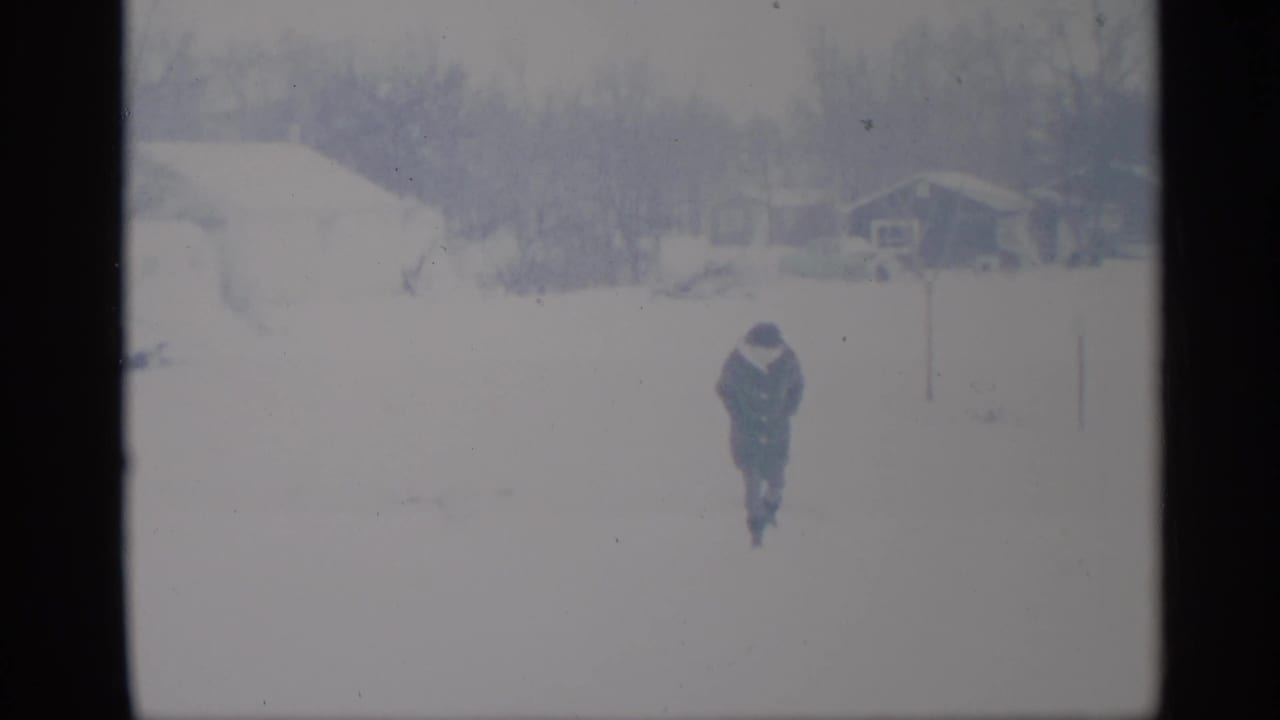 Distant person walking through a snow-covered yard toward the camera.