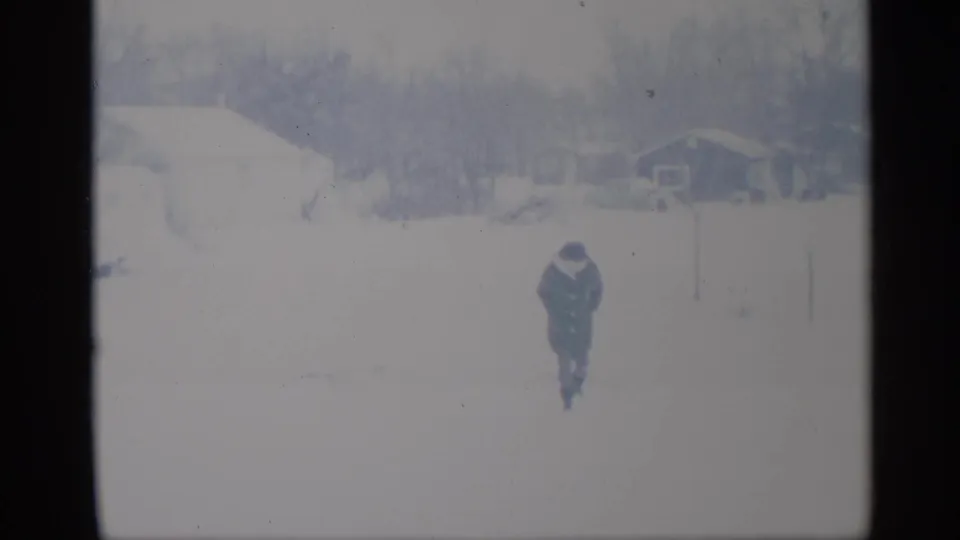 A person walks across a snowy residential yard in New York, consistent with 1959 8mm home-movie footage.