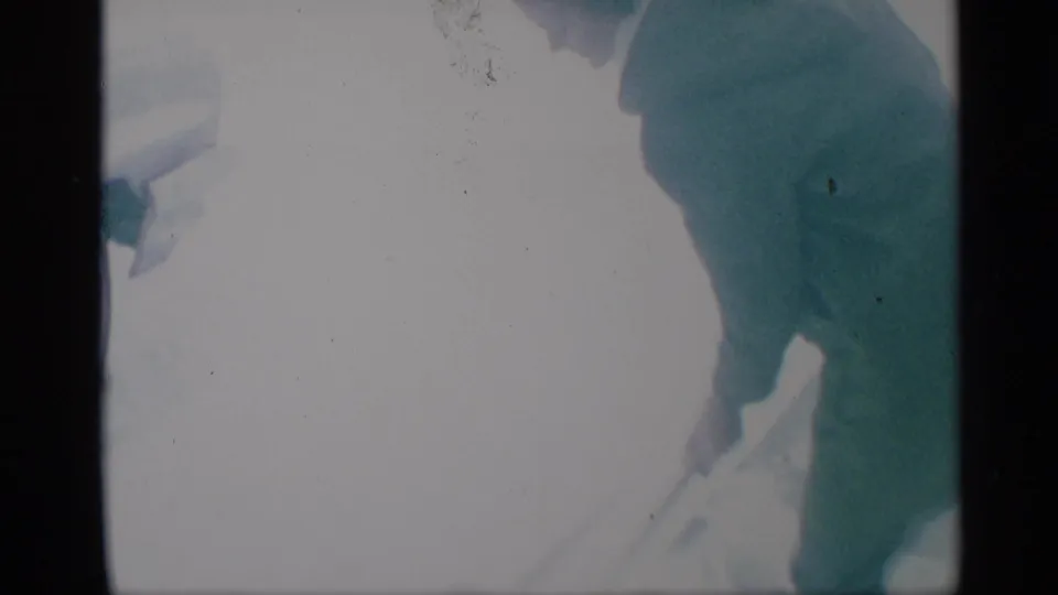 A tightly cropped 8mm frame shows the woman’s coat and shovel during snow clearing, with her head partly outside the visible image area.