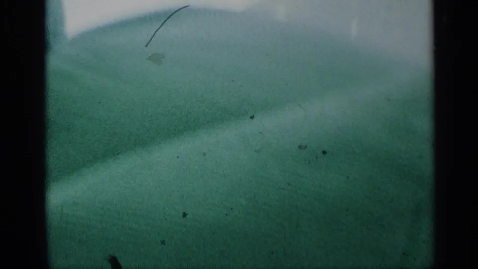 Distant bridge span over water, likely the Mackinac Bridge per metadata, seen in hazy blue-green 8mm footage.