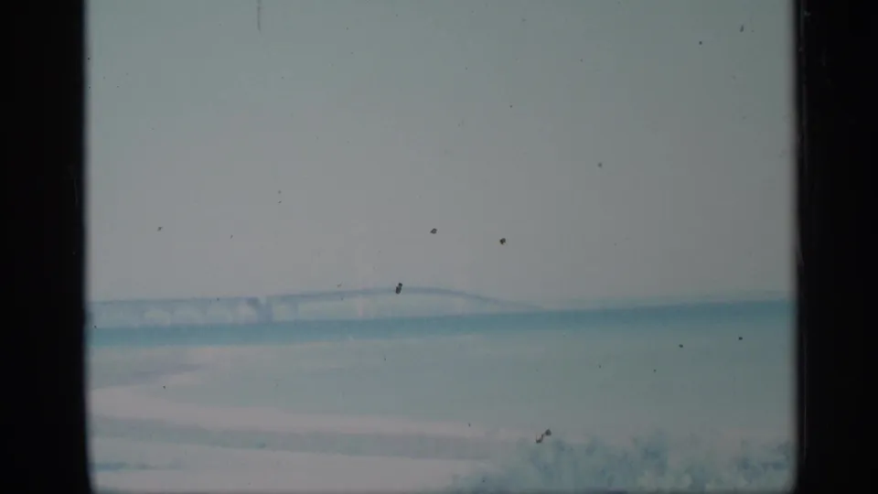 1959 New York 8mm frame showing a wide, washed-out waterfront with a low distant bridge shape.