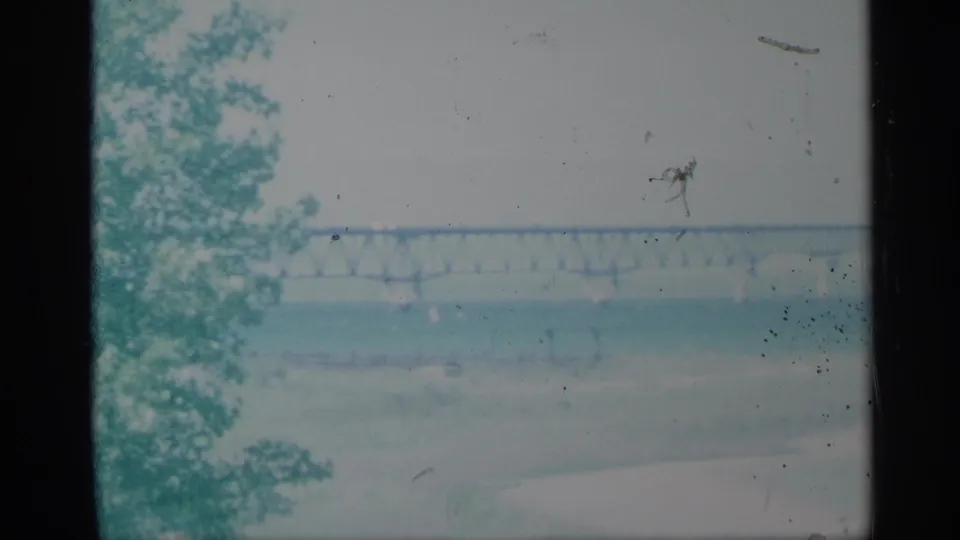 1959 New York 8mm frame with a steel truss bridge across water and a leafy tree along the left foreground.