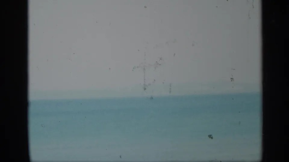 1959 New York home-movie frame with calm water, hazy sky, and a dark central vertical obstruction.