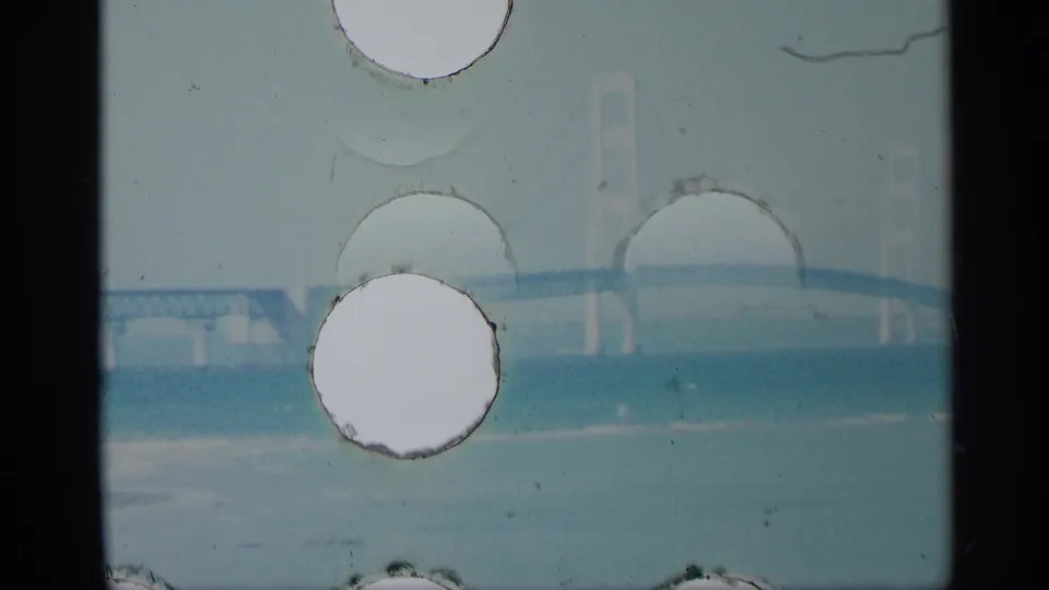 1959 New York 8mm frame with a distant bridge over blue water, partly hidden by circular film damage and scratches.