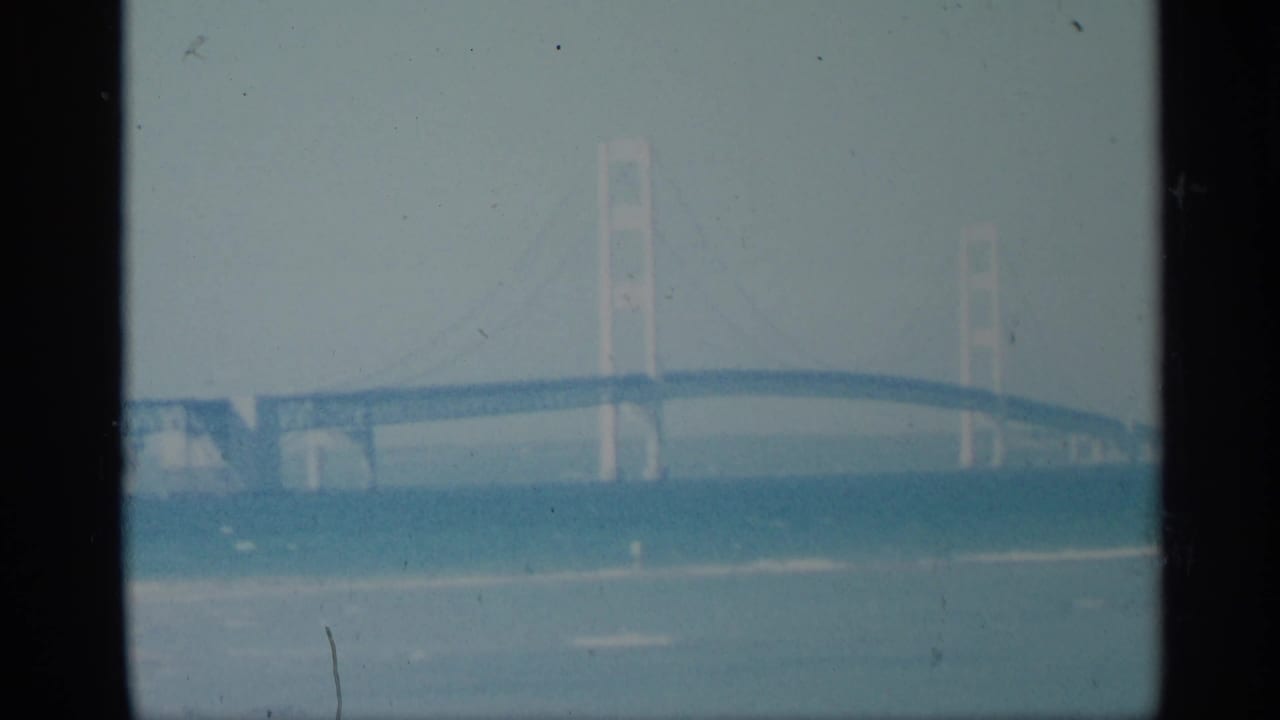 Hazy suspension bridge spanning blue water with dark film gate borders.