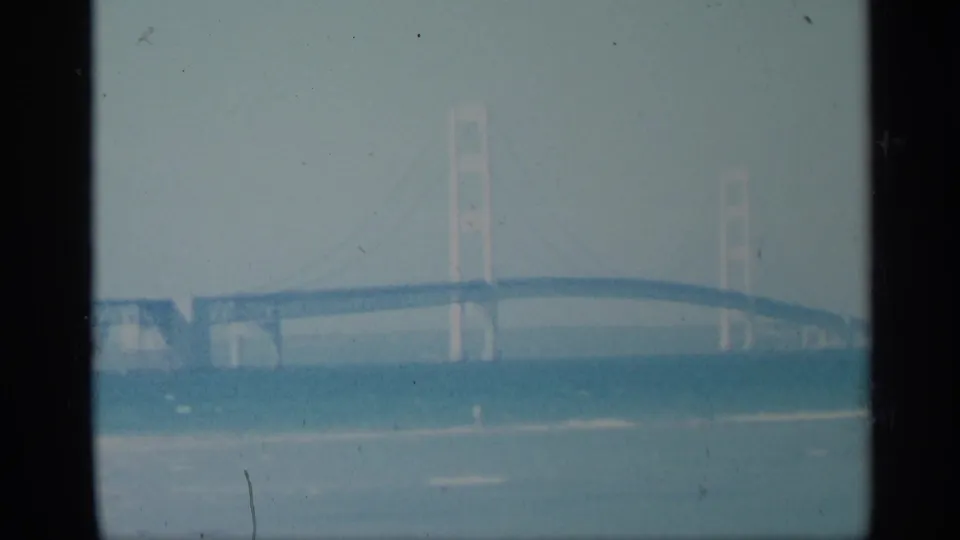 1959 8mm frame showing a long suspension bridge across open water, with faded color and visible film wear.