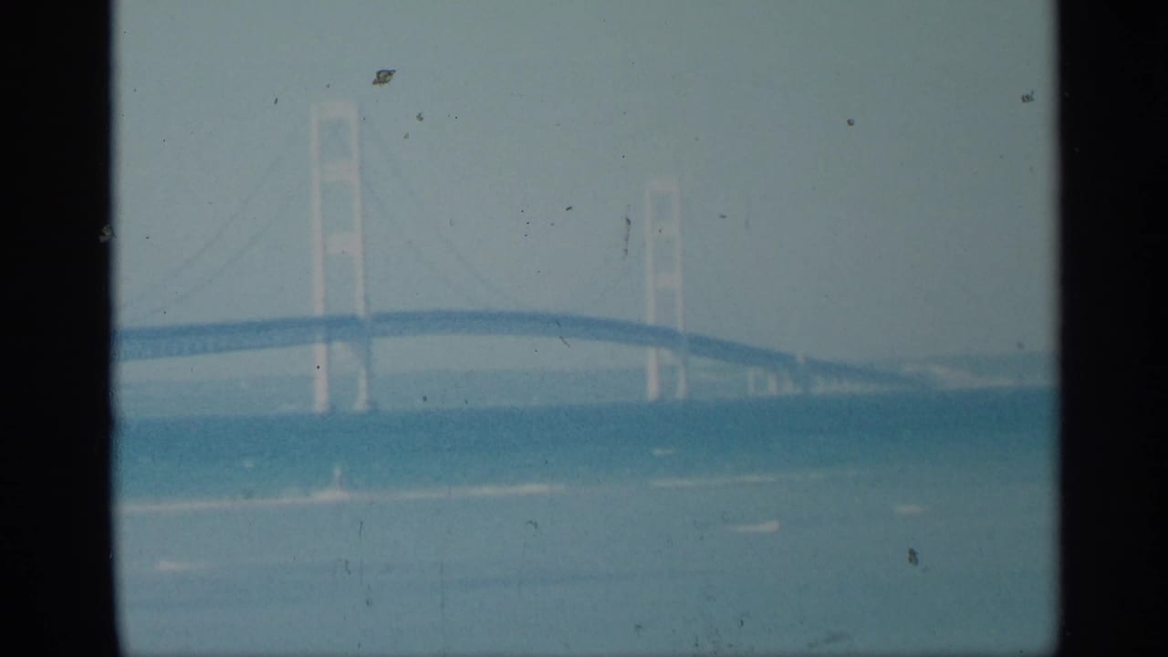 Distant suspension bridge over water, framed by heavy vertical film edges.