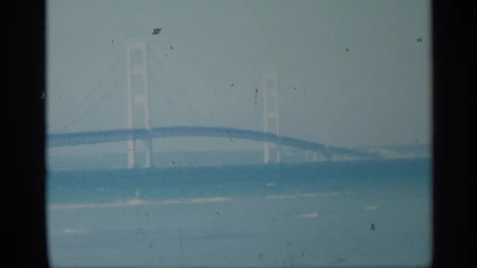 A soft, faded 8mm view of a large suspension bridge crossing blue water, with gate edges and speckling visible.