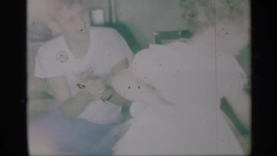 Soft, overexposed 8mm home-movie frame showing two young people close together, with faces partially visible.