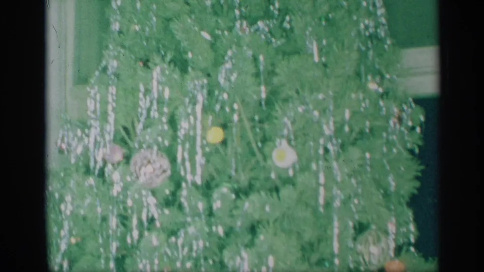 Close 8mm view of the decorated Christmas tree with tinsel, colorful ornaments, and a partial interior edge at the side.